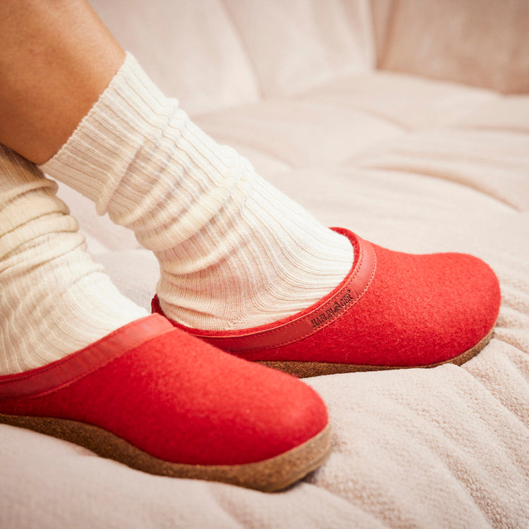 Person wearing white socks and bright red slippers sits on a light-colored cushioned surface.